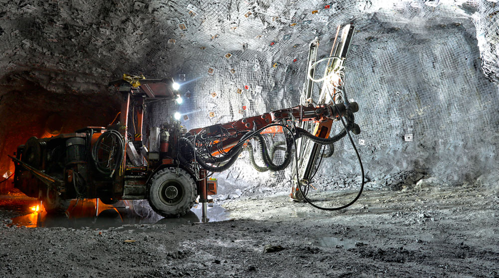 A mining drilling jumbo operating inside an illuminated underground tunnel.