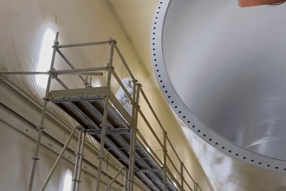 Worker applying industrial coating inside a storage tank using airless spray equipment